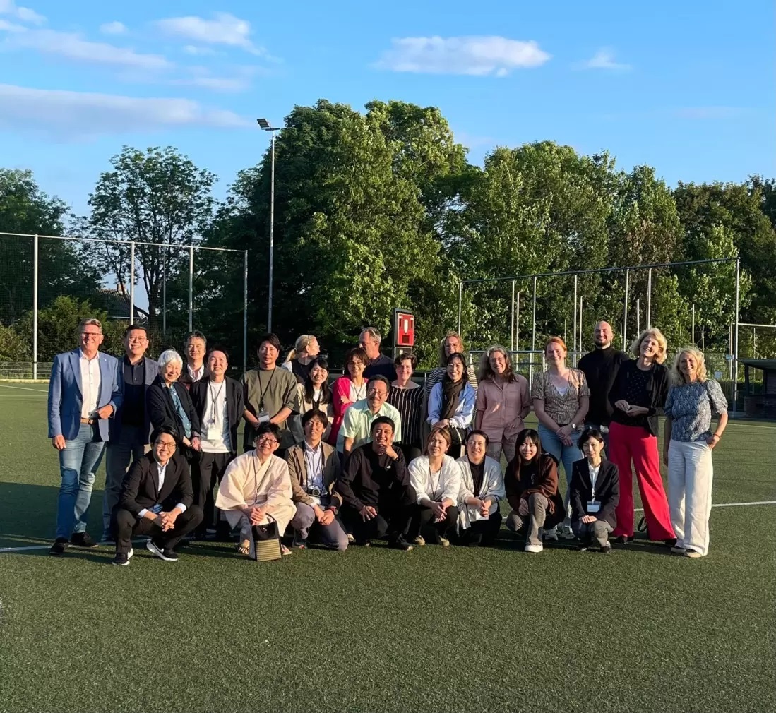 Een groep artsen uit Japan in het grasveld bij een voetbalvereniging, samen met collega's van de gemeente en wethouder Gerben van Duin