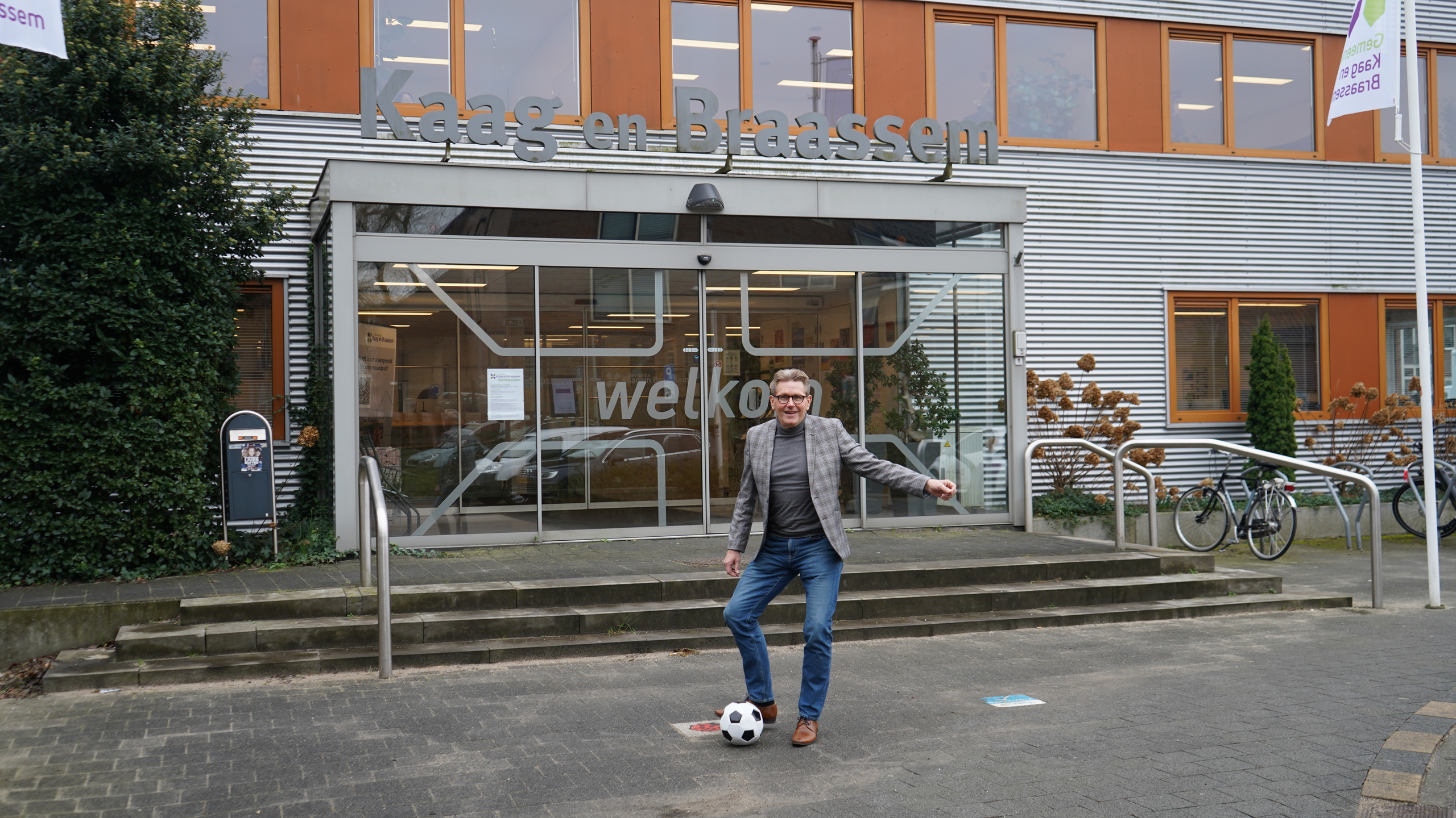 Wethouder Gerben van Duin trapt een balletje voor het gemeentehuis, namens het Sportfonds